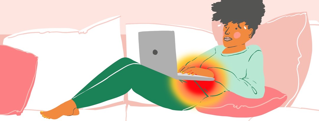 A stressed woman works on a laptop while sitting with her legs up on her couch, while a red dot over her abdomen indicates an IBS flare.