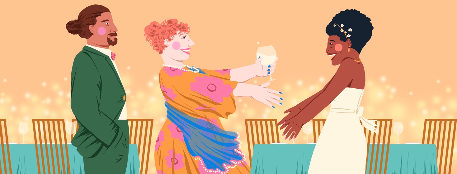 A delighted woman extends her arms to another happy woman in a wedding dress. The first woman also has a glass of white wine in her hand. A smiling man is standing behind the first woman. Beyond the trio are tables set with plates and wine goblets, and soft lights are lit in the background.