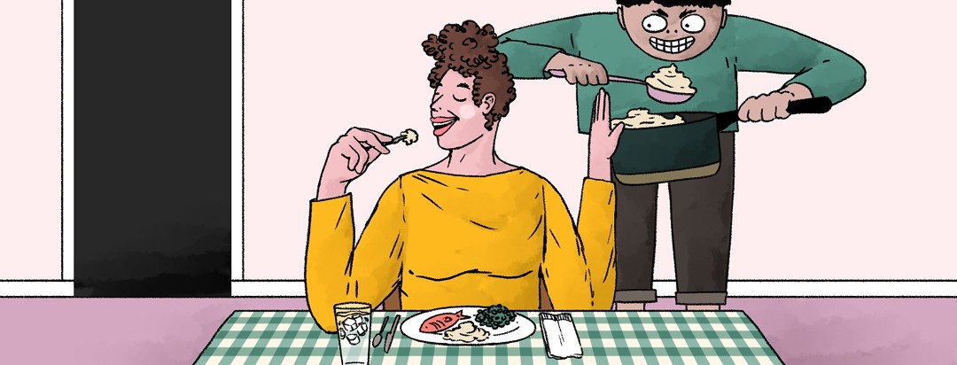 A woman sits at a dinner table smiling and putting her hand up at a menacing figure behind her that is trying to give her another serving of food.