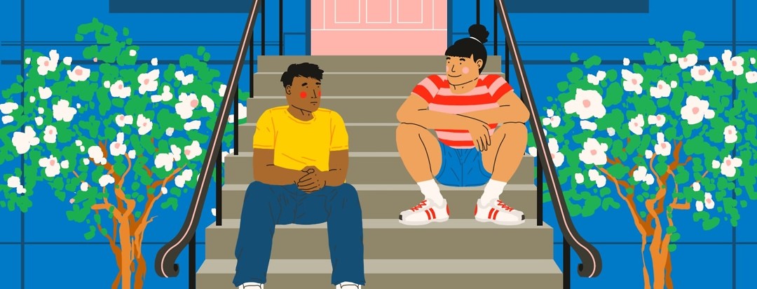 Two people are sitting on the stoop of a brownstone. One is squatting and one is sitting more like you would in a chair.
