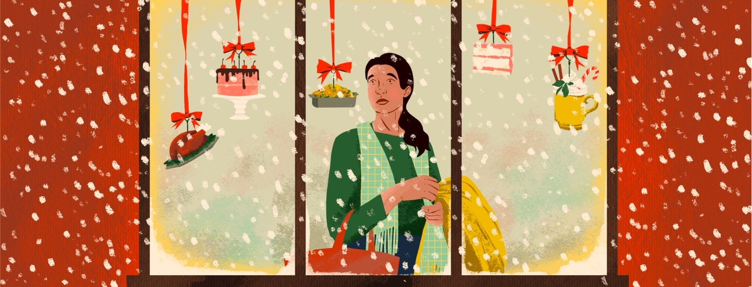 A woman is viewed through a store window. She is holding a bag and jacket and looking sadly at blown glass ornaments hanging in the window depicting different kinds of decadent foods. It is snowing outside the window.