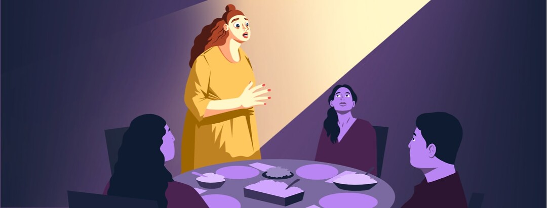 A woman stands up from a dinner table where she is sitting with three other people. She is speaking passionately and illuminated by a spotlight.