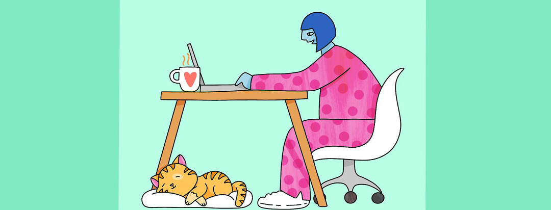 A woman in pajamas sitting at a computer desk with a cat peacefully sleeping at her feet.