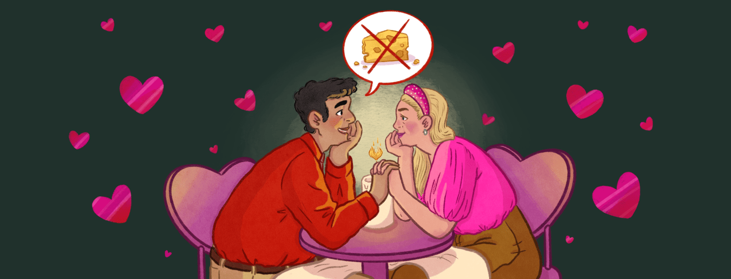 A male and a female hold hands across a table with their chins resting on their other hands, a candle between them has a heart shaped flame, the man has a speech bubble coming from his mouth of cheese with an x over it, they are sitting on heart shaped chairs and hearts are floating around them