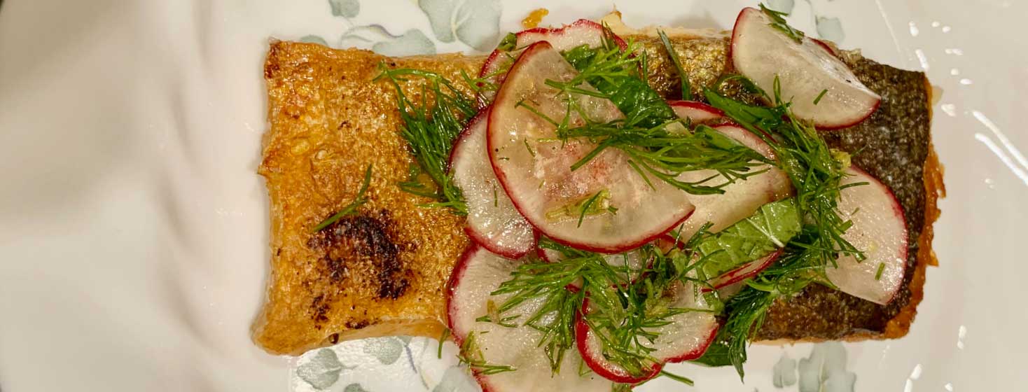 Salmon topped with radish and herb salad on a plate
