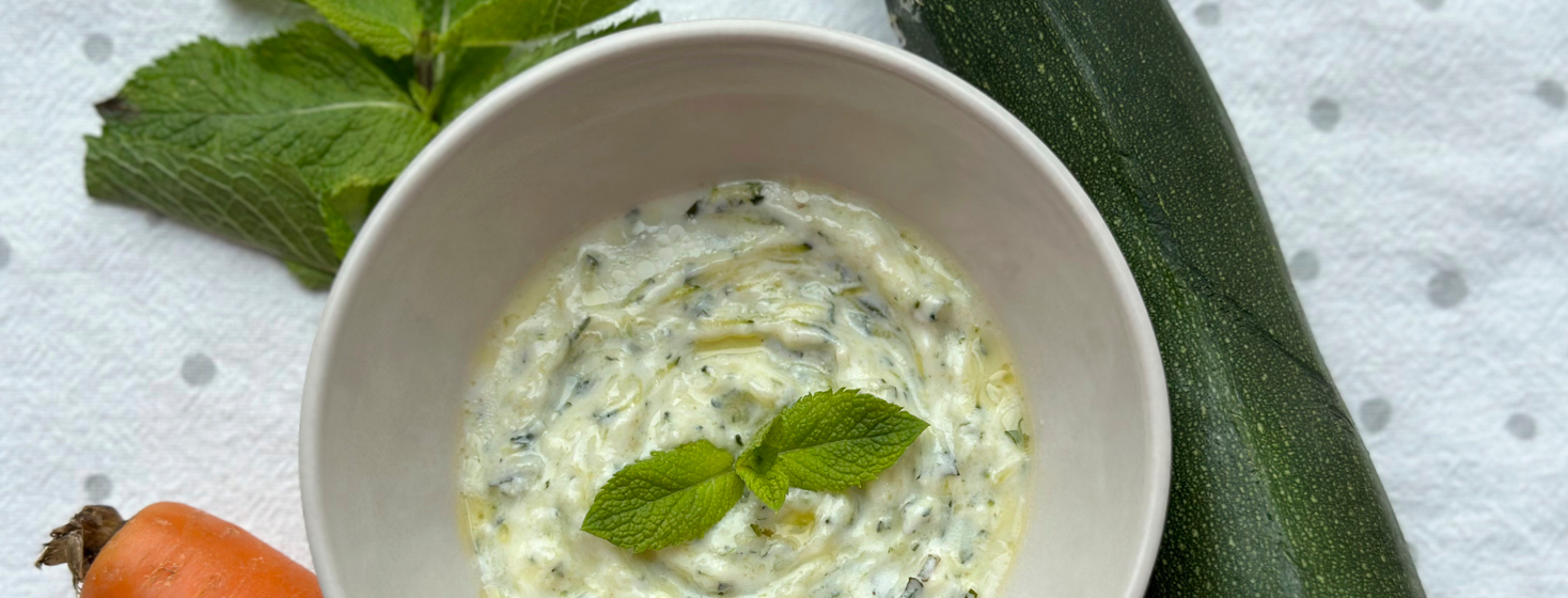 Bowl of creamy sauce with spices and garnish surrounded by vegetables