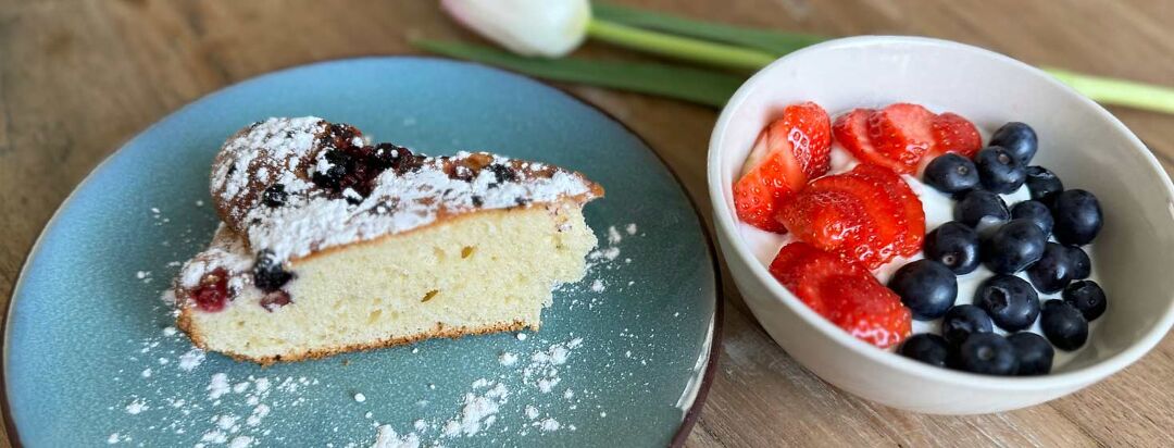 A plate of fluffy yogurt cake alongside a bowl of yogurt with berries on top.